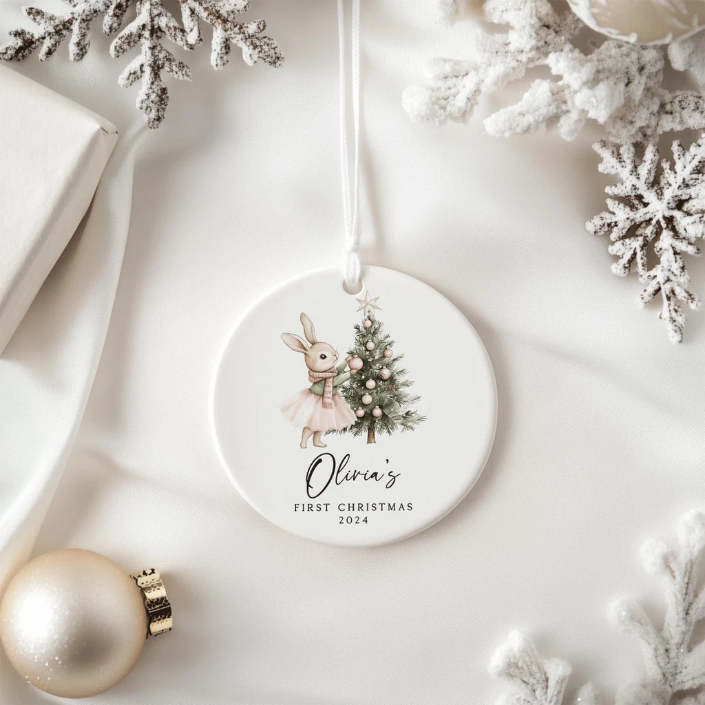 Round Christmas ornament with a rabbit and tree design, featuring 'Olivia's First Christmas 2024', on a white background with decorative elements.