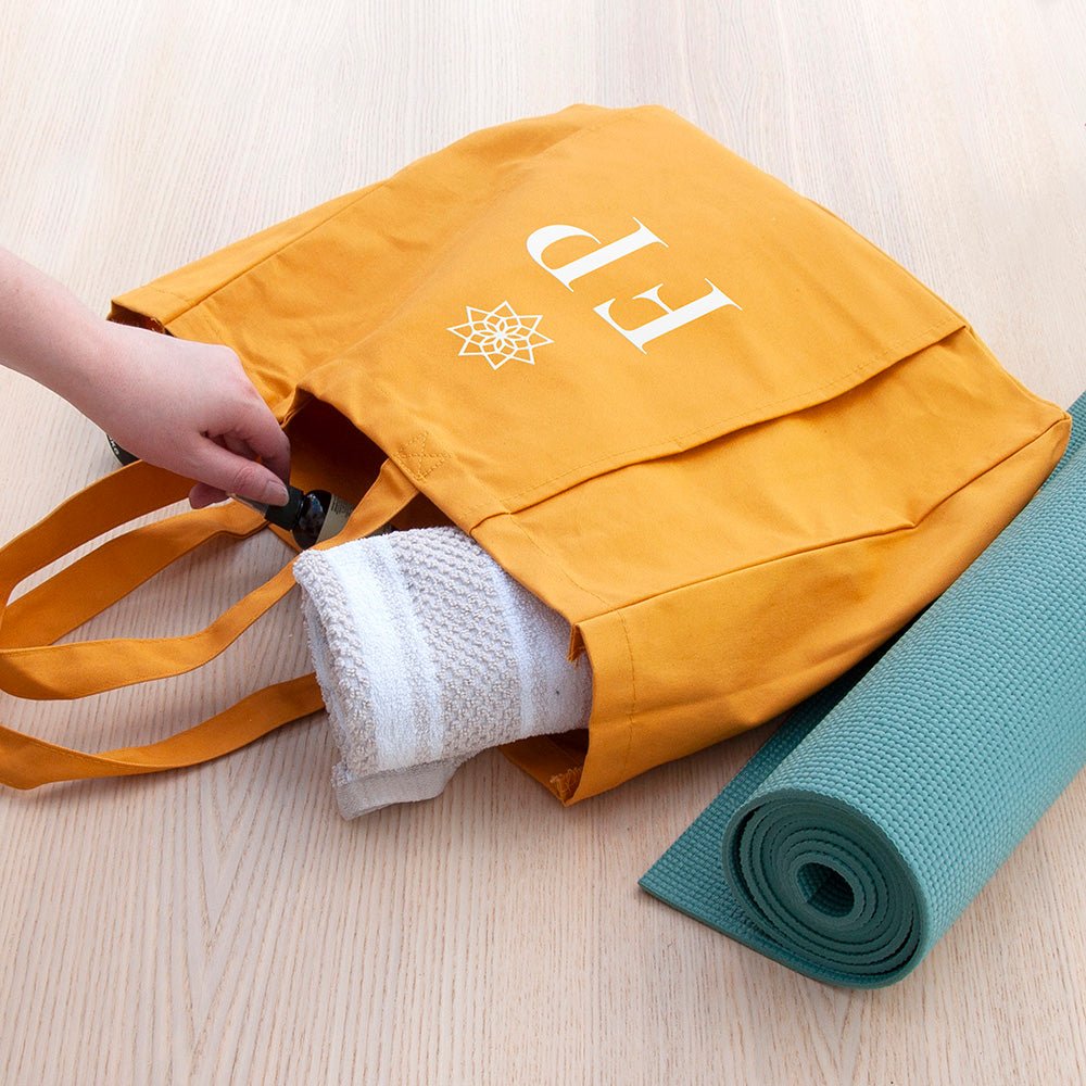 Yellow tote bag with rolled-up yoga mat and towel on a light wooden surface