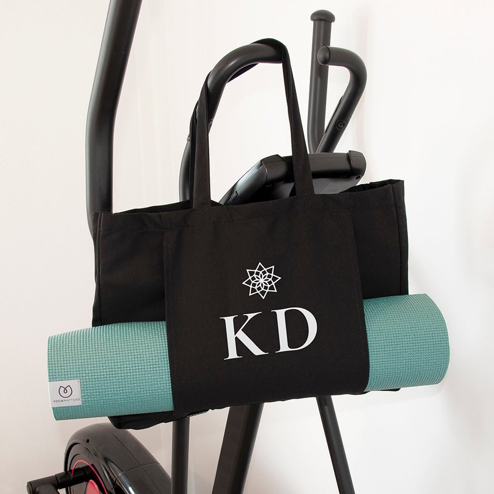 Black tote bag with 'KD' monogram and teal yoga mat on a white background