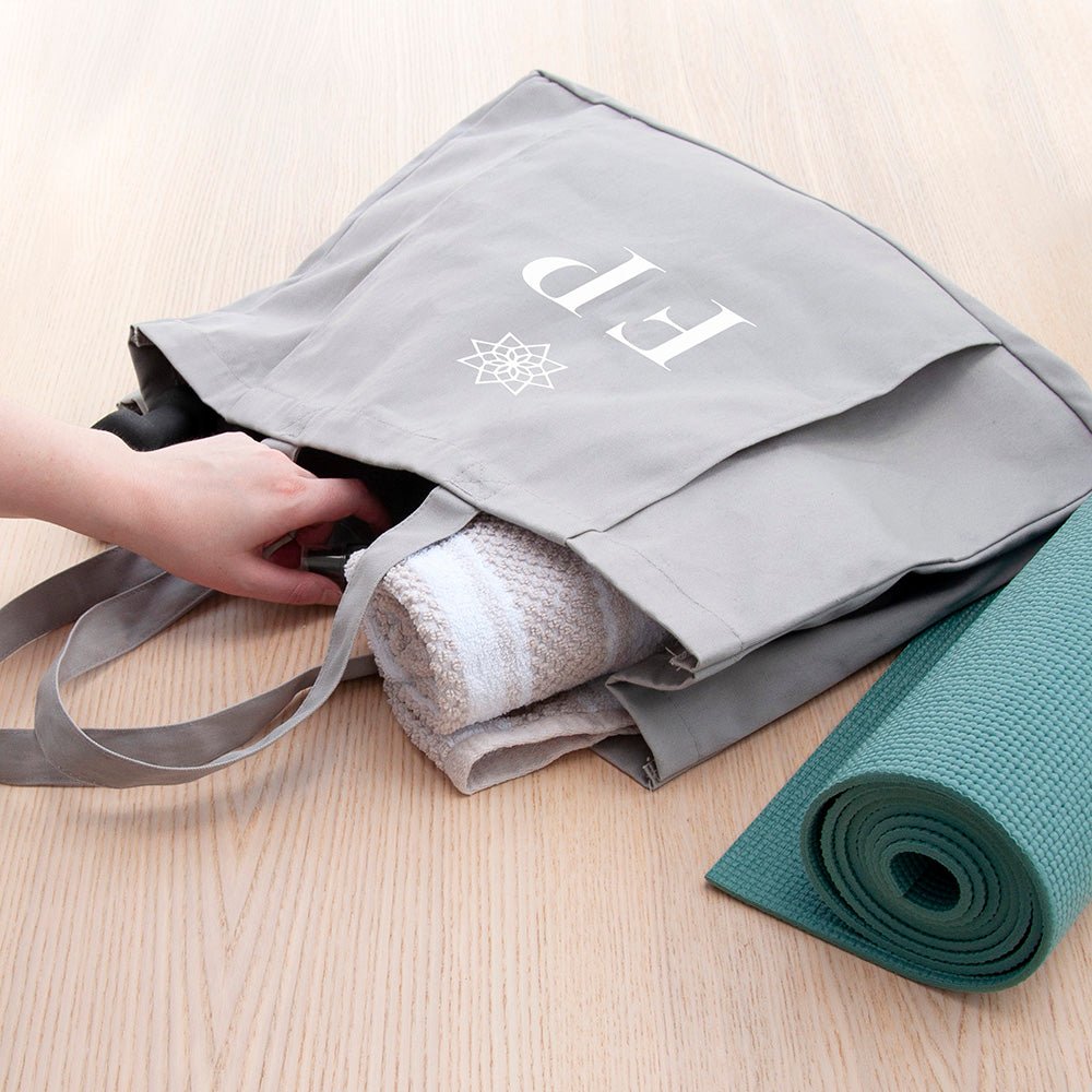 Gray tote bag with rolled towel and yoga mat on a light wooden surface