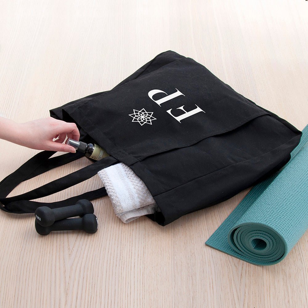 Black tote bag with rolled-up yoga mat and accessories on a light wooden floor