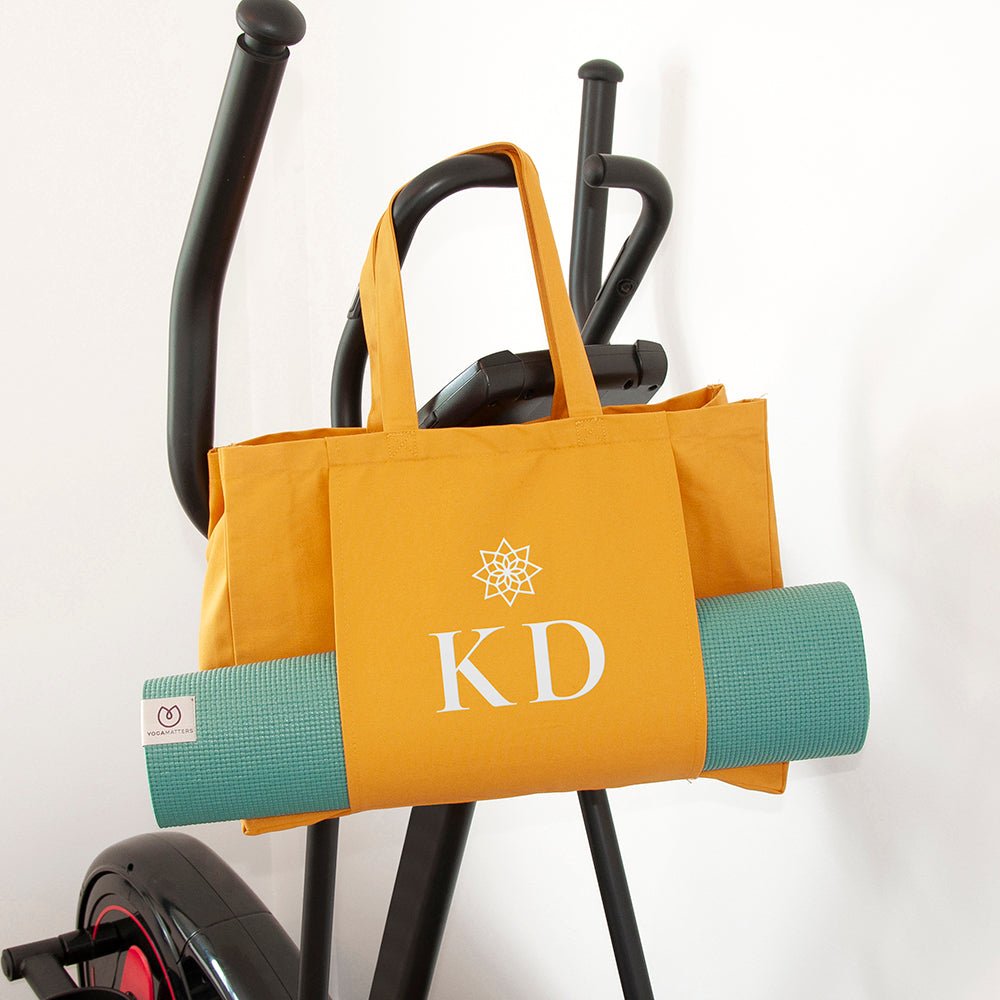 Yellow tote bag with 'KD' logo and green yoga mat on a white background