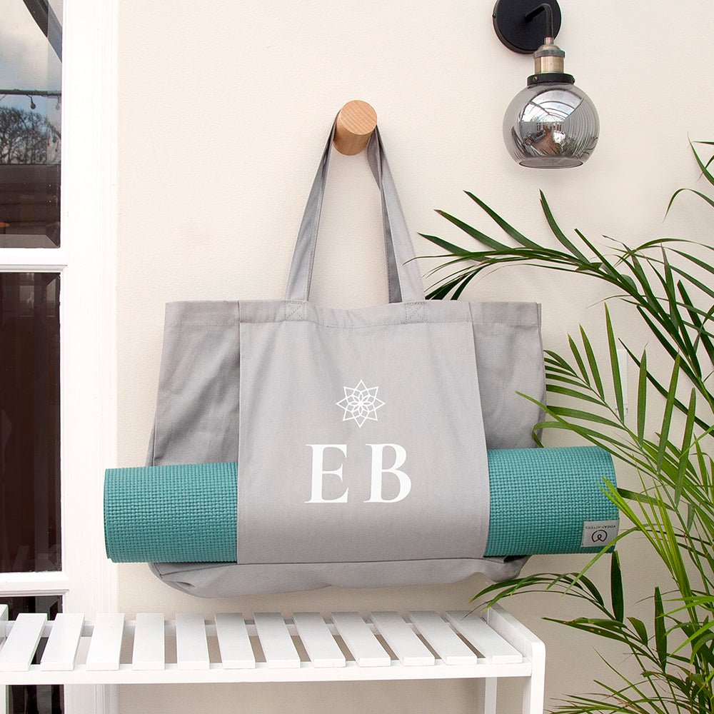 Gray tote bag with 'EB' initials and a teal yoga mat on a white shelf.
