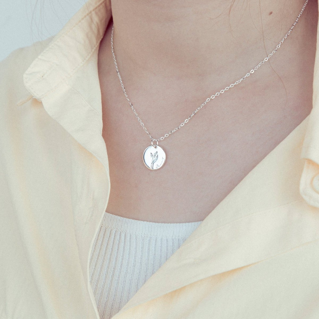 Silver necklace with a pendant worn by a person in a light-colored outfit.