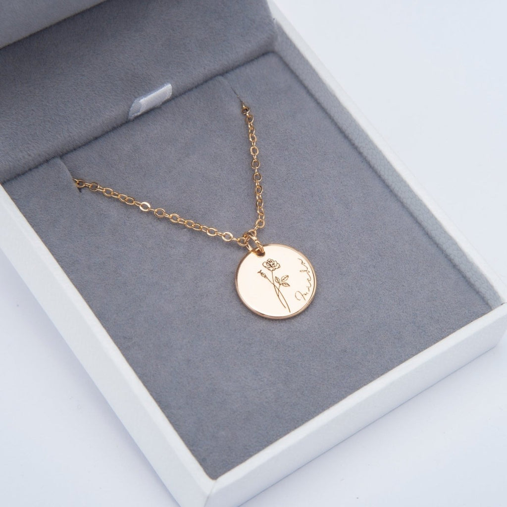 Gold necklace with a round pendant featuring a floral design on a gray cushion in a white box. engraved memories