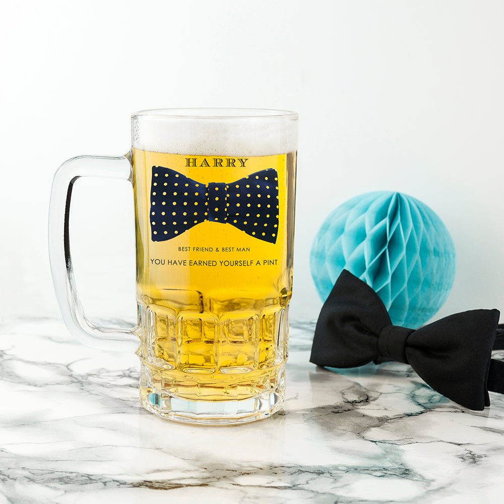 Glass mug with beer and a bow tie design, placed on a marble surface with a blue decorative ball.