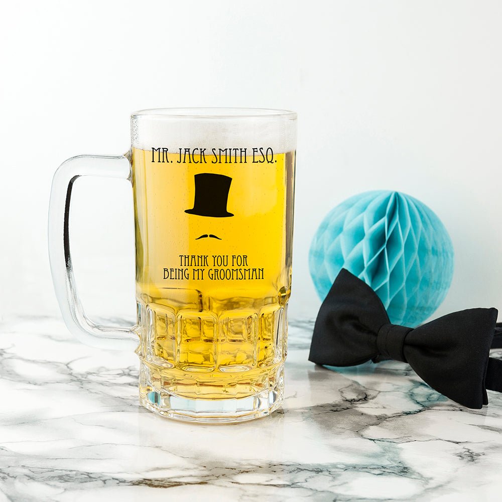 Personalised glass mug with yellow liquid and text, accompanied by a black bow tie on a marble surface.