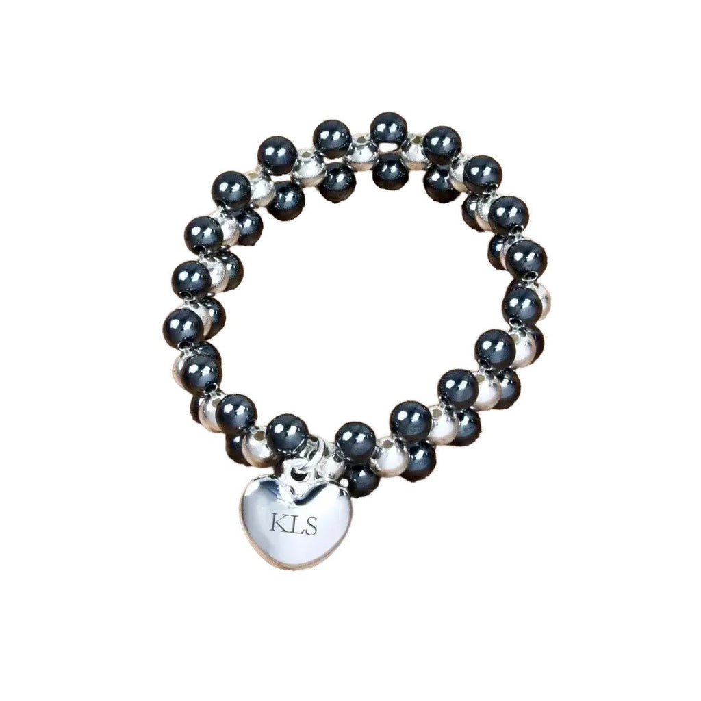 Beaded bracelet with a heart-shaped charm labeled 'KLS' on a wooden surface