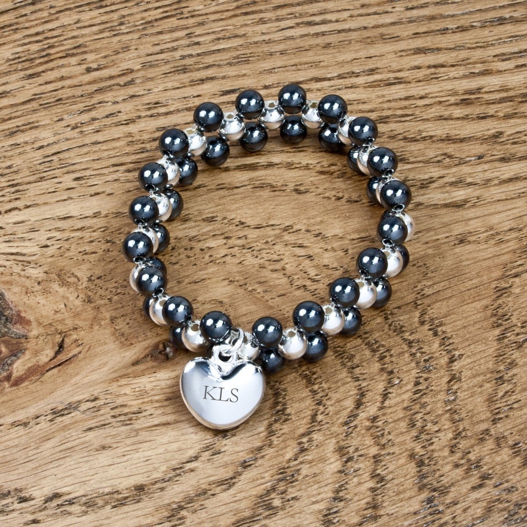 Beaded bracelet with a heart-shaped charm labeled 'KLS' on a wooden surface