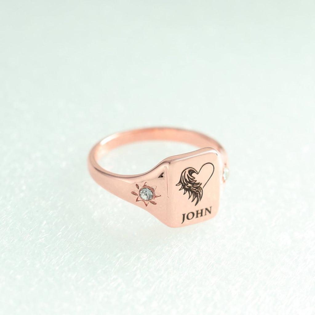 Rose gold ring with engraved design and 'JOHN' on a light green background