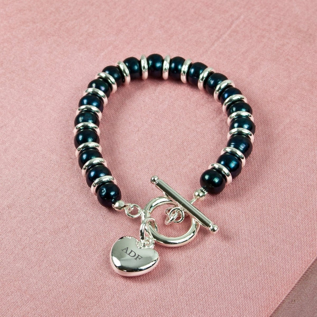 Black beaded bracelet with silver toggle clasp and heart-shaped tag on pink fabric background