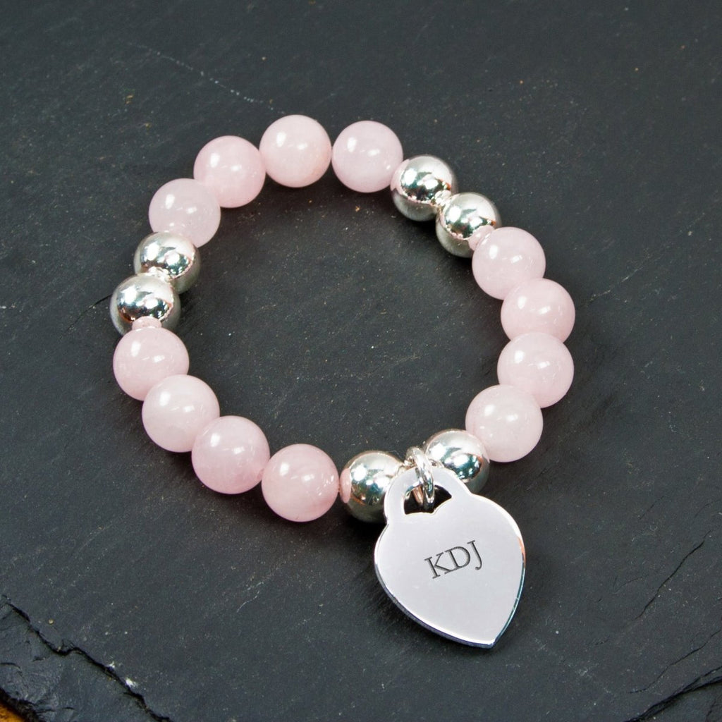 Pink beaded bracelet with a silver heart charm on a dark surface