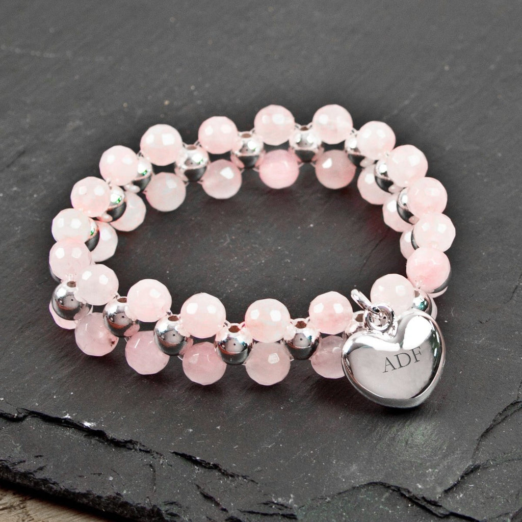 Pink beaded bracelet with a silver heart charm on a dark slate surface