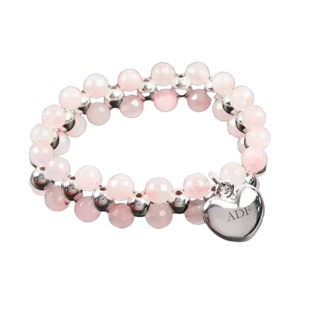 Pink beaded bracelet with a silver heart charm on a dark slate surface