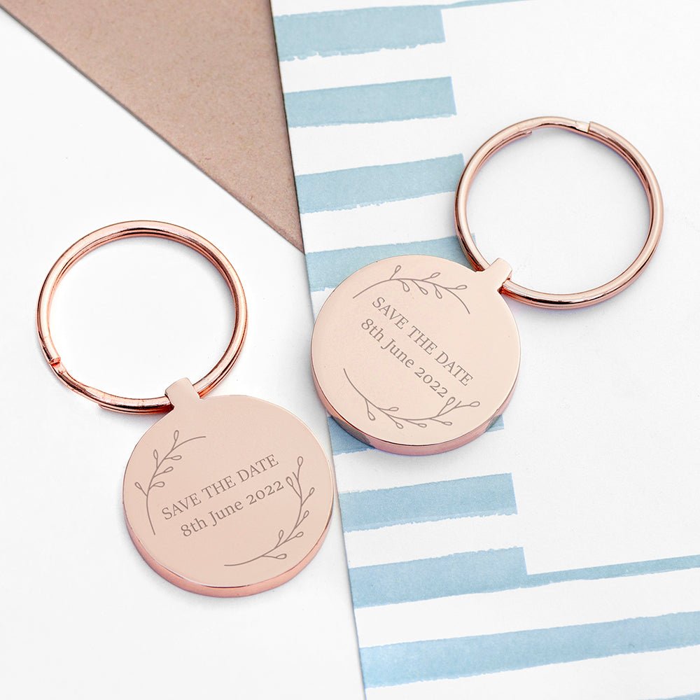 Two rose gold keychains with 'Save the Date' engraving on a striped background