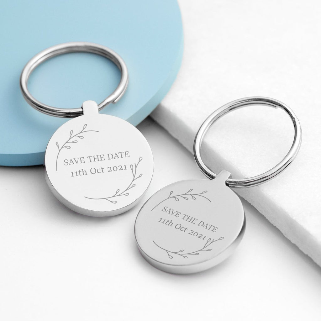 Two silver keychains with 'Save the Date' engraving on a light blue and white background
