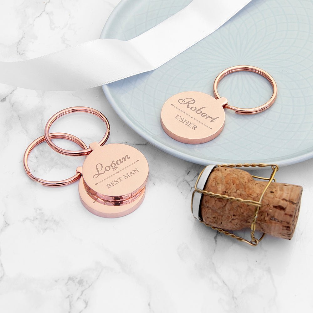 Rose gold keychains with engraved names on a marble surface.