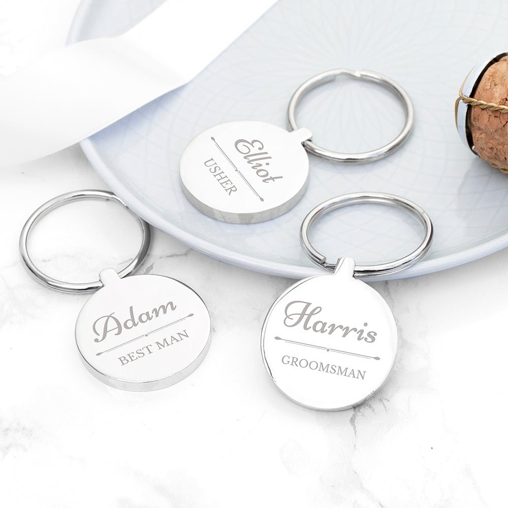 Three silver keychains with engraved names on a marble surface.