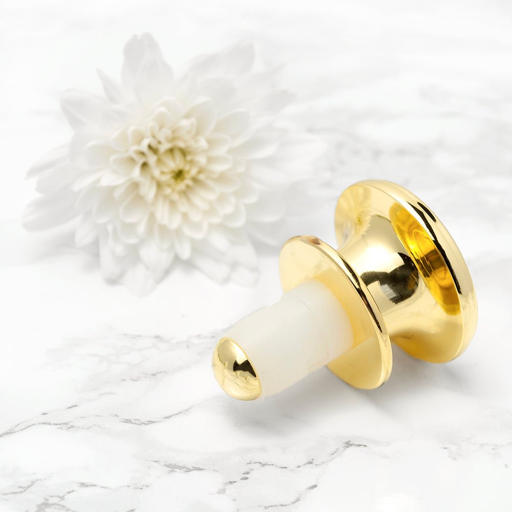Gold and white cylindrical object on a marble surface with a white flower in the background